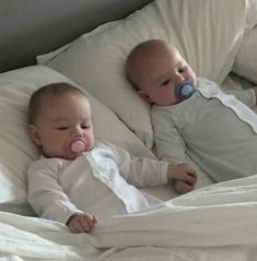 two baby babies laying on top of a bed next to each other with pacifier in their mouths