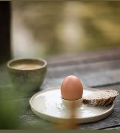 an egg sitting on top of a plate next to a piece of bread and a cup of coffee