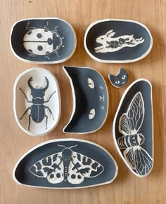 six ceramic dishes with bugs and moths painted on them, sitting on a wooden surface