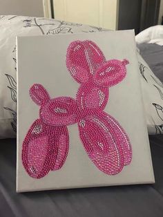 a painting with pink beads on it sitting on top of a bed next to pillows