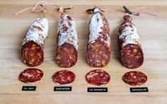 four different types of salamis on a wooden cutting board with labels for each