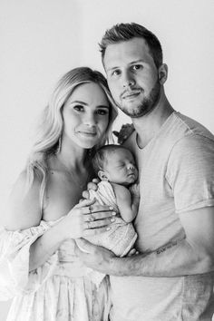 a man and woman holding a baby posing for a black and white photo with the baby in her arms