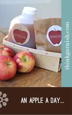 an apple cider and two apples in a wooden crate on a table with paper bags