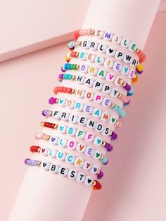 a stack of bracelets with words written on them sitting on a pink surface next to a white object