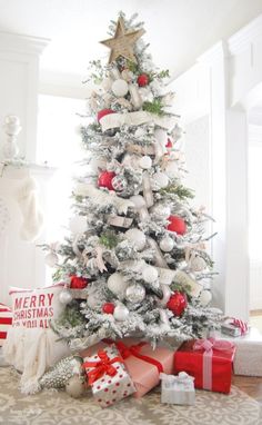 a white christmas tree with red and silver presents on the floor in front of it