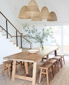 a dining table with four stools under some hanging lights in a white walled room