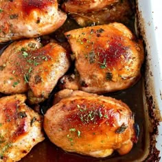 chicken thighs in a baking dish with gravy and herbs on the top, ready to be cooked