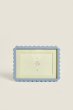 a blue and white frame with an embroidered flower on the bottom, sitting in front of a gray wall