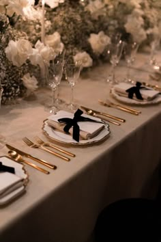 the table is set with white flowers and gold place settings