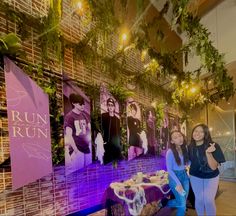 two women standing next to each other in front of a wall with pictures on it