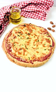 a pizza sitting on top of a white table next to a jar of olive oil