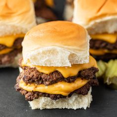 two cheeseburger sandwiches sitting next to each other on top of a black surface