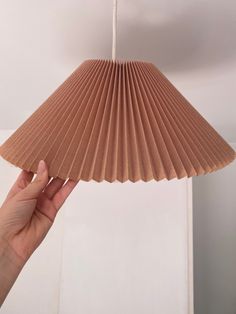 a hand is holding up a brown paper lamp shade that looks like a pleated fan