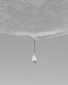 a drop of water that is dripping from a faucet on a gray background