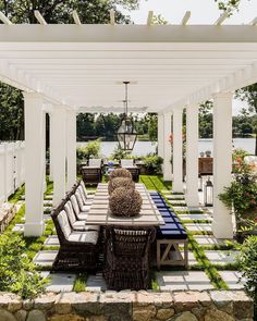 an outdoor dining area with white pergoline and stone walls, surrounded by greenery