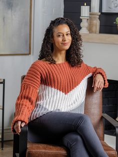 a woman sitting in a chair wearing an orange and white sweater