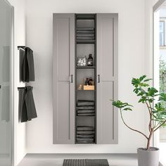 a white bathroom with grey cupboards and towels on the shelves next to a potted plant