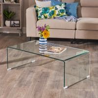 a glass coffee table with flowers on it in front of a couch and bookshelf