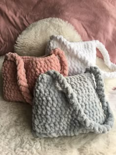 three crocheted purses sitting on top of a white fluffy bed next to a pink pillow