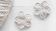 two crocheted flowers next to a ball of yarn on a white wooden surface