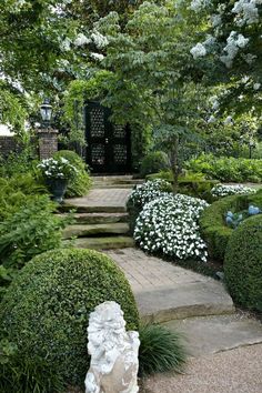 a stone statue sitting in the middle of a garden filled with trees and bushes, surrounded by white flowers