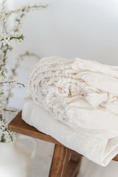 a stack of white blankets sitting on top of a wooden bench next to a vase with flowers