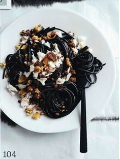 a white plate topped with pasta covered in toppings next to a fork and spoon