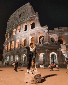 two people standing on top of a rock in front of an old building at night