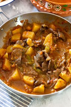 a stew with potatoes and meat in a pan on a table next to other dishes