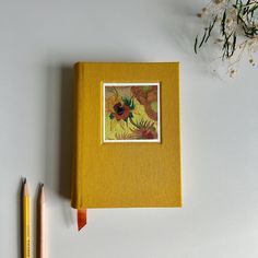 a yellow book sitting on top of a table next to two pencils and a plant