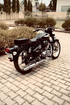 a black motorcycle parked on top of a cobblestone road next to shrubbery