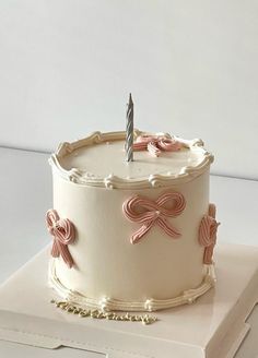 a white cake with pink bows and a single lit candle on top is sitting on a stack of books