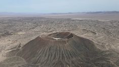 an aerial view of a large crater in the middle of desert land with mountains and blue sky