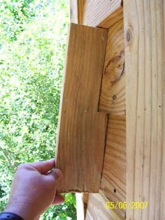 a person is holding up a piece of wood to the side of a wooden structure