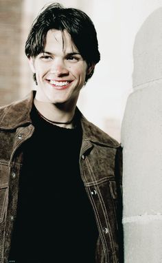 a smiling young man leaning against a wall