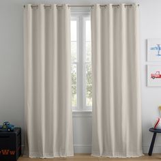 a white curtain hanging on the side of a window next to a wooden chair and table