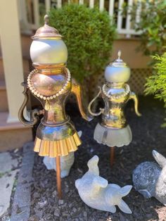 two metal teapots sitting next to each other on top of a gravel ground