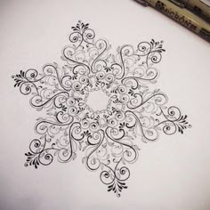 a drawing of a snowflake with swirls and scrolls on paper next to a marker