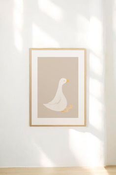 a white duck sitting on top of a wooden floor in front of a framed wall