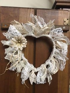 a white wreath is hanging on a wooden door with lace and burlock around it