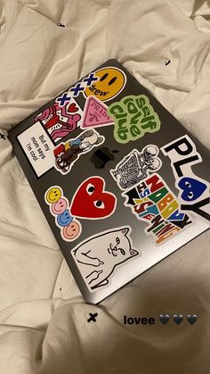 an open laptop computer sitting on top of a bed covered in white sheets and stickers