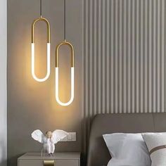 two lights hanging from the ceiling above a bed in a room with grey walls and pillows