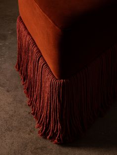 an orange velvet couch with fringes on the bottom and back end, sitting in a dark room