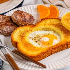 an egg is in the middle of toast on a plate with sausages and orange slices