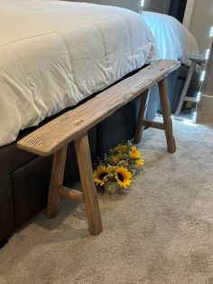 a wooden bench sitting on top of a bed next to a white comforter and flowers