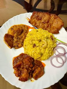 a white plate topped with meat and rice covered in sauces next to onion rings