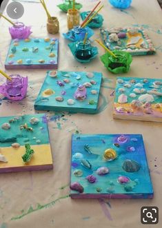 the table is covered with paintings and seashells on canvases that are being painted