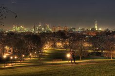 the city lights shine brightly in the distance as people walk on a grassy field at night