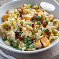 a white bowl filled with macaroni salad on top of a wooden cutting board