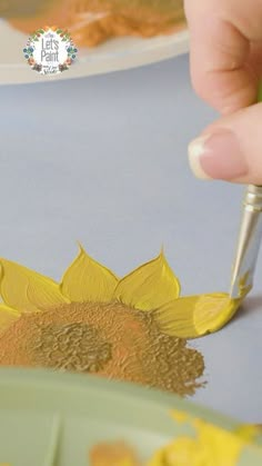 someone is painting a sunflower on the table with yellow paint and a green brush